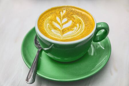Ayurvedic turmeric latte coffee cup. Golden milk froth with turmeric powder coloring anti-inflammatory food detox.の写真素材