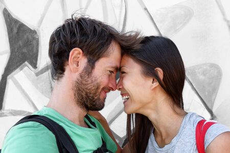 Interracial couple young happy Asian woman and Caucasian man lovers smiling laughing kissing portrait. Tourists on travel holiday taking phone selfie picture hugging each other.の写真素材