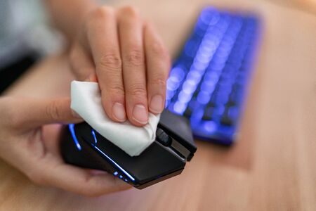 Coronavirus COVID-19 sanitize disinfecting wipes cleaning disinfection of work mouse. Wiping with antibacterial wipe the surface of desk, keyboard, at office against corona virus COVID-19.の写真素材