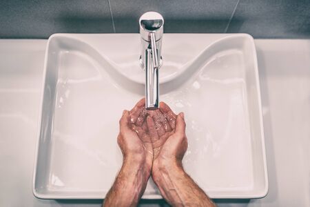 Washing hands with soap at work bathroom sink man hand care hygiene for coronavirus outbreak prevention. Corona Virus pandemic precaution by washing hands frequently for 20 seconds.の写真素材