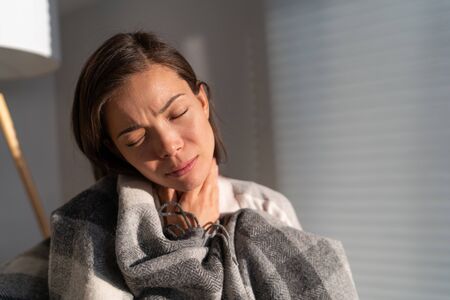 Coronavirus disease (COVID-19) symptoms are a runny nose, sore throat, cough, and fever. Corona virus illness can be more severe for some people. Asian woman with throat pain at home.の写真素材