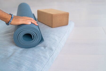 Yoga exercise mat fit woman hand with mala bracelet rolling fitness object on wellness accessories. Workout at home: meditation pillow, cork block prop on wooden floor.の写真素材