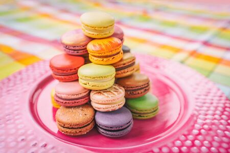 Macarons tower on dessert plate at home. Cute retro vintage pink plate on checkered tablecloth easter table decoration home kitchen. Assortment of pastel colored macaron of different flavors.の写真素材