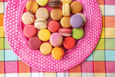 Many french macarons selection of colorful pastries on pink dessert plate top view. Retro vintage...