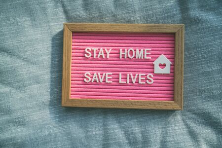 Coronavirus quote stay home, save lives pink felt board sign with message of self isolation for social responsability on home sofa background. COVID-19 text to promote staying at home.の写真素材
