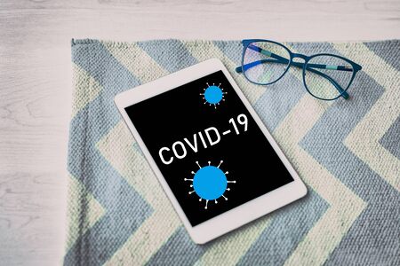 Corona virus news online read at home on tablet. Top view of COVID-19 text written on black...