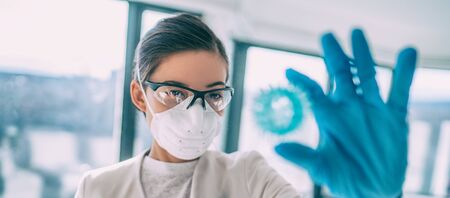 COVID-19 researcher looking at virus model in search of a cure. Coronavirus lab research woman vaccine holding corona virus blue sphere of COVID-19. Panoramic banner.の写真素材