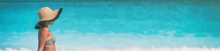 Caribbean beach woman tourist travel relaxing on vacation banner panorama blue ocean background. Sun tan hat.の写真素材
