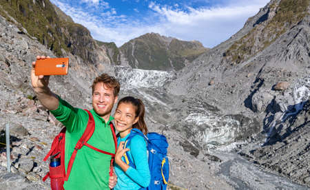 Selfie couple taking phone self-portrait on New Zealand by Franz Josef Glacier. New Zealand tourists smiling happy in nature by Franz Josef Glacier, Westland Tai Poutini National Park.の写真素材