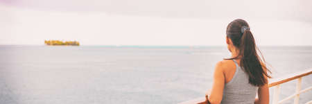 Travel woman on cruise ship deck watching sunset crusing on ocean looking at island away. young tourist girl from behind relaxing on boat yacht deck outside on tropical luxury getaway banner panorama.の写真素材