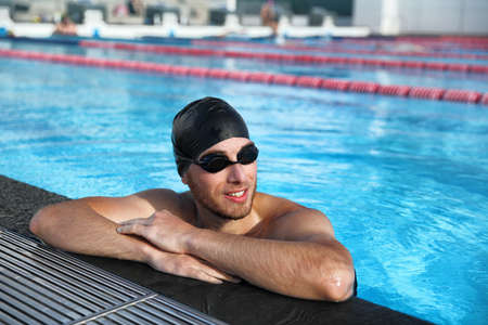 Professional sport swimmer athlete portrait at swimming pool. Active lifestyle healthy fit man wearing cap and goggles.の写真素材
