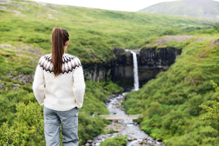 Iceland. Woman hiking looking at Svartifoss waterfall. Female is visiting famous tourist attraction of Iceland. Spectacular natural landmark on vacation in Skaftafell. Icelandic nature landscape.の写真素材