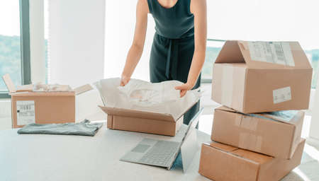 Selling clothing from home. Small business entrepreneur woman packing dress clothes in mailing box...
