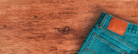 Jeans pants on wooden banner panoramic background. Top view of brown wood texture and blue denim clothing for men and women showing leather back label.の写真素材