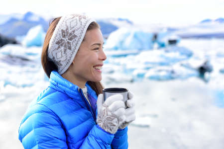 Woman drinking coffee outside in winter landscape wearing winter clothing. Portrait of smiling happy...