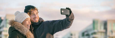 Winter selfie couple tourists on city travel vacation taking photo with mobile phone in street...