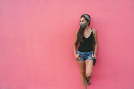 Asian woman leaning on pink wall wearing fabric face mask in fashion leopard pattern print. Casual...