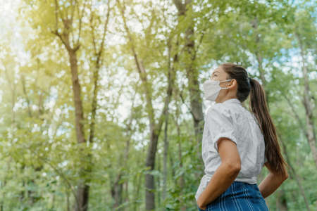 Eco-friendly sustainable face mask. Woman wearing kn95 korean masks walking in outdoor forest lookin up at sunlight. Hope concept for environment. Coronavirus covering.の写真素材