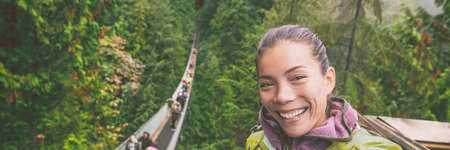 Canada travel tourist woman taking selfie photo at Capilano Suspension Bridge in Vancouver, British Columbia, canadian vacation destination for tourist. Asian girl talking to camera phone.の写真素材