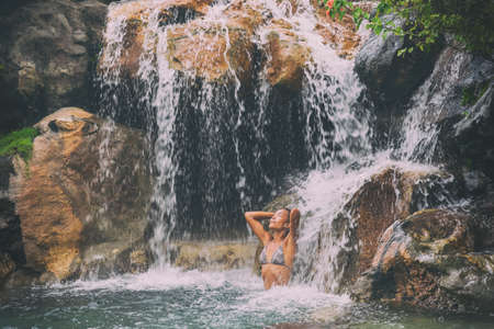 Waterfall woman relaxing in wellness nature water in tropical travel vacation background. Sexy bikini body care girl swimming in natural pool. Health and spa concept.の写真素材