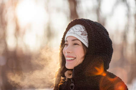 Winter cold Asian woman breathing in cold air with dewy mist clouds against sunlight in forest nature walk outdoor lifestyle. Happy people life style outside.の写真素材