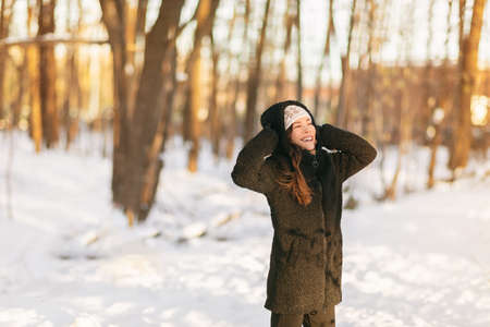 Winter snow fun happy girl walking outside in cold weather protecting ears holding wool hat over...