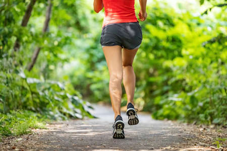 Runner running legs from the back jogging on nature path outside. Running shoes girl training cardio...