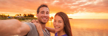 Happy selfie couple tourists banner panorama vacation taking photo at sunset on Florida beach....