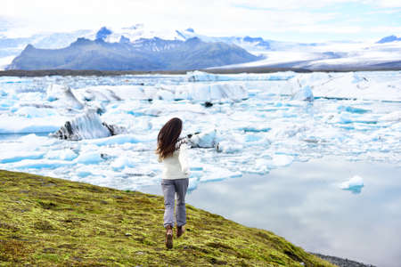 Iceland travel tourist joyful and happy running having fun in Jokulsarlon glacial lagoon / glacer lake on Iceland. Woman outdoors by tourist destination landmark attraction.の写真素材