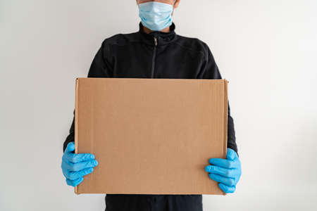 Online food delivery man delivering at home door cardboard box parcel wearing protective glove and mask ppe prevention for COVID-19.の写真素材