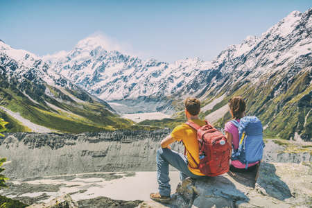 Backpackers couple hiking looking at Mount Cook view on mountains tramping in New Zealand. People hikers relaxing during hike in alps of south island.の写真素材