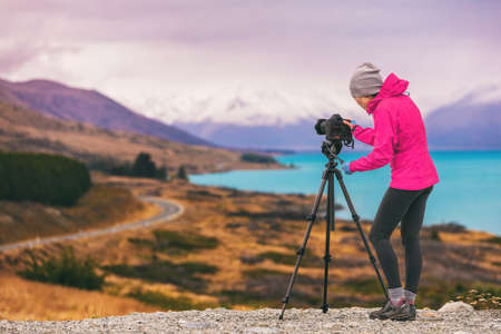 Travel photographer woman shooting nature photography mountain landscape at Peters lookout, New Zealand. Girl tourist on adventure holiday with photo equipment, slr camera on tripod at dusk.の写真素材