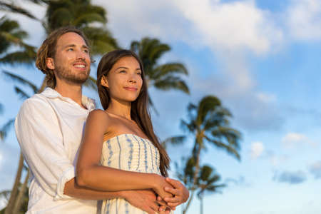 Relaxing couple watching sunset on summer travel vacations. multiracial people enjoying tropical holiday together hugging in love.の写真素材