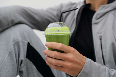 Green smoothie detox man drinking vegetable juice cleanse. Sport athlete holding plastic cup breakfast drink closeup.の写真素材