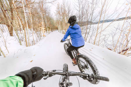 Couple biking on fat bikes on winter snow trail outdoor. Mountain nature landscape, woman rider...