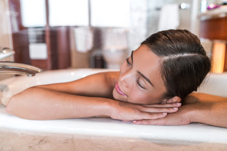 Woman relaxing in bathtub at home taking hot bath wellness alone time. Asian lady happy sleeping in...