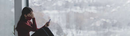 Depressed woman using phone alone at home during coronavirus pandemic panoramic banner. Anxiety, depression, grief mental heatlh concepts.の写真素材