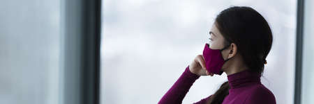 Asian woman wearing mask during coronavirus pensive thinking about anti-asian hate crimes on the rise in society because of corona virus racism. Panoramic banner.の写真素材