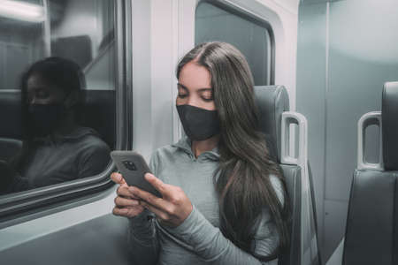 Public transport commute woman commuter at night wearing face mask riding subway using mobile phone....