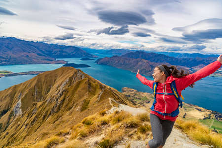 Travel post Covid-19 concept. Pent-up traveling demand concept. Hiker jumping of joy funny - woman hiking in New Zealand laughing having fun, joyful and aspirational at Roys Peak, South Islandの写真素材