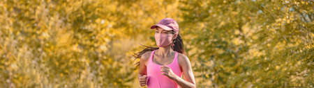 Happy running woman training wearing face mask on autumn yellow background bannerの写真素材