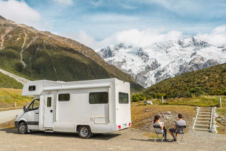 Motorhome camper van RV road trip on New Zealand. Couple on travel vacation adventure. Tourists looking at view of Aoraki Mount Cook National park and mountains on pit stop next to their rental carの写真素材