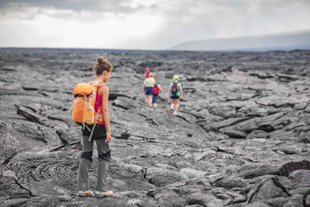 Hiking group of hikers walking on Hawaii volcano lava field hike adventure happy woman with backpack in Big Island, Hawaii. Tourists walking on guided tour trail outdoor USA summer travel vacationの写真素材