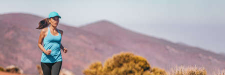 Trail runner summer Asian athlete woman running outdoor on mountain trail. Fitness active healthy lifestyle sports girl wearing cap for sun protection. People training in desert landscape bannerの写真素材