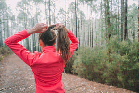 Runner woman getting ready to run pulling hair to do a ponytail preparing for long distance trail running in outdoor forest nature. Girl athlete from behind preparation for fitness workout motivationの写真素材
