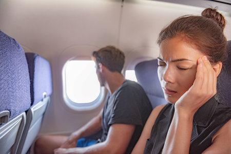 Sick woman in airplane fear of flying inside plane cabin with headache. Asian passenger on travel feeling sick with stress anxiety migraine. Couple tourists.の写真素材