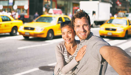 New York travel selfie tourists couple taking photo on NYC city street summer holiday vacation with yellow taxi cabs in the background. Man and woman friends having funの写真素材