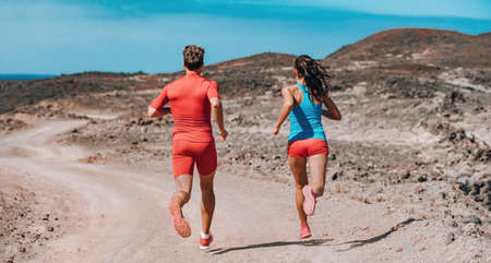 Trail running couple on outdoor exercise. Rear view of athletes sprinting away fast on summer mountain training. Two runners workoutの写真素材