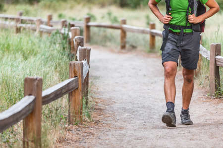 Hiker with backpack walking on hiking path trail in nature woods. Crop of mans legs with shoes on summer travelの写真素材