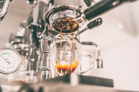 Coffee maching making espresso shot in naked bottomless portafilter at home kitchen. Beautiful crema pouring in transparent double wall glassの写真素材